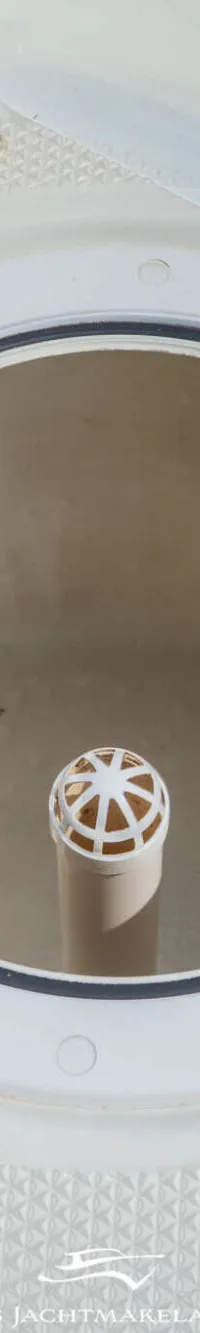 Een open rond luik met een zwarte rubberen rand en een witte buis met een geperforeerde bol in het midden.
