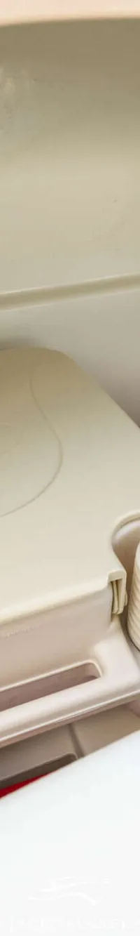 Een draagbaar toilet met toiletpapier in een plastic zak, opgeborgen in een witte opbergruimte.