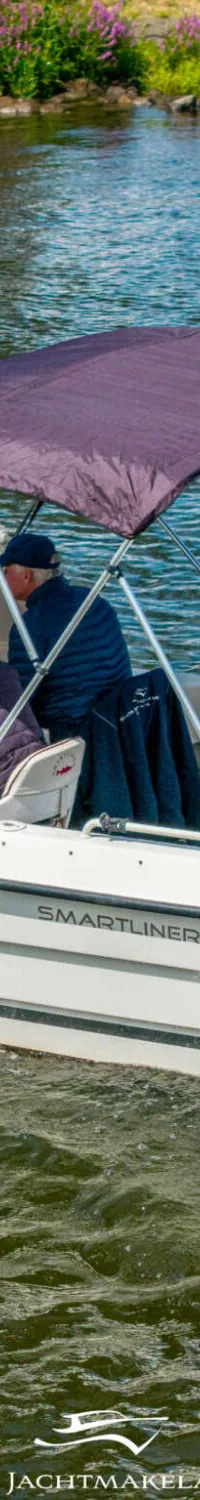 Een witte boot met twee personen aan boord vaart op het water, met een paarse biminitop en een Mercury buitenboordmotor.
