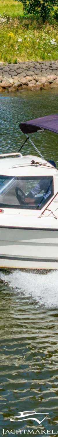 Een witte motorboot met een paarse biminitop vaart over het water, met een persoon aan boord.