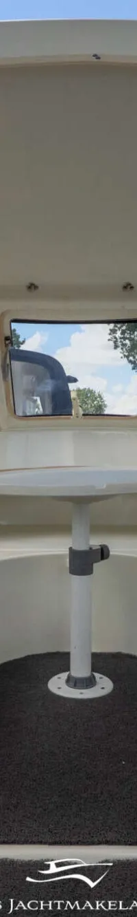 De foto toont het interieur van een boot met een stuurwiel, een tafel en zitplaatsen, gezien vanuit de achterkant.