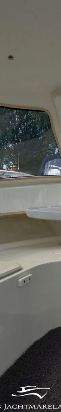 Een interieur van een boot met een witte tafel, grijze vloerbedekking en ramen die uitzicht bieden op bomen en een blauwe…