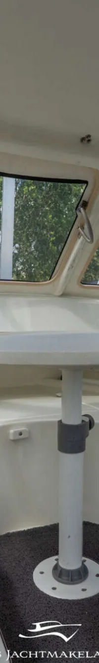 De foto toont het interieur van een boot met een tafel, ramen, een stuur en een Garmin-apparaat.