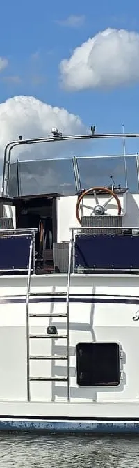 Een witte motorboot met de naam "Pannerden" op de spiegel, een zwemtrap en een stuurwiel op het bovendek.