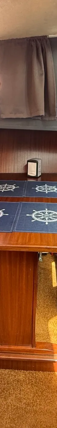 De foto toont een kajuit met een houten tafel en twee banken met blauwe kussens, omringd door houten panelen.