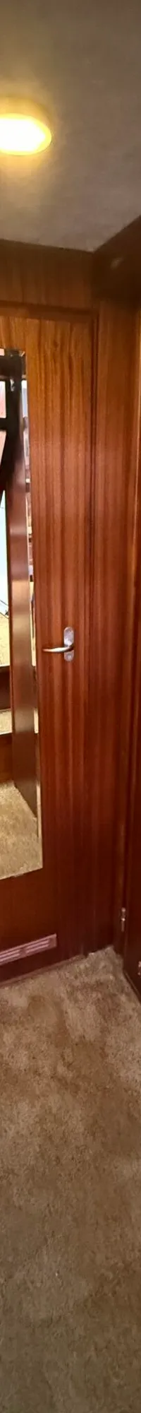 Een gang met houten wanden en deuren, een bruine vloerbedekking, en een spiegel die een trap weerspiegelt.