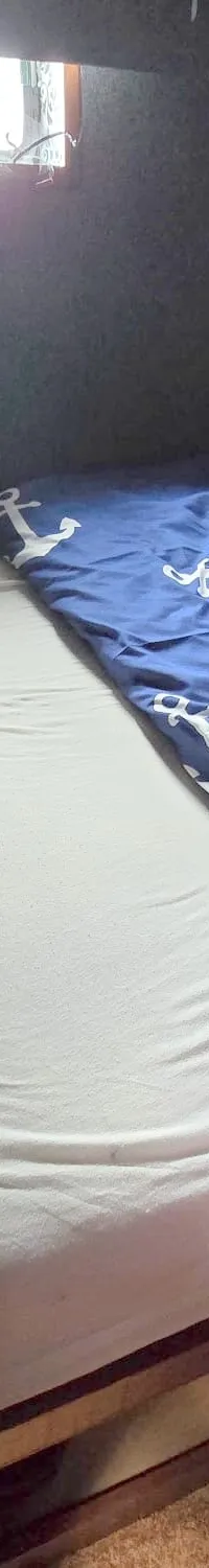 Een kajuit met een bed met wit hoeslaken, een blauw dekbed en kussen met ankerpatroon, en een klein raam.