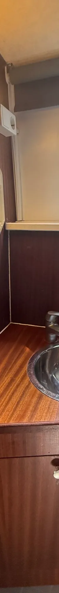 Een houten badkamer met een spiegel, wastafel, kraan, twee ramen en een lamp.