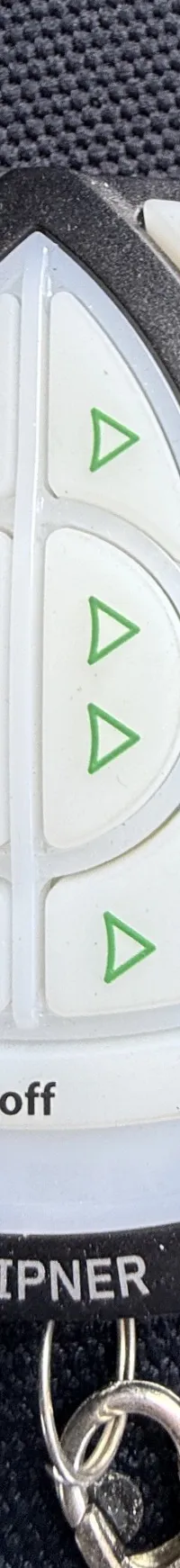 Een zwarte afstandsbediening met witte knoppen en rode en groene pijlen ligt op een donkere, gestructureerde ondergrond.