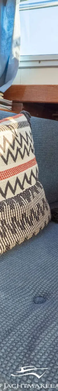 Een interieur van een boot met houten wanden, een blauwe bank met een patroon kussen, en een raam met gordijnen.