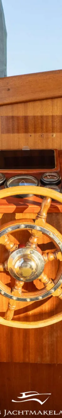 Een houten stuurwiel en bedieningspaneel in een boot met een tafel en zitplaatsen op de achtergrond.