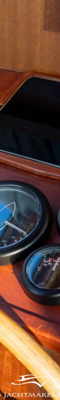 Een houten stuurwiel, diverse meters, een tablet, schakelaars en een gashendel zijn zichtbaar op een houten dashboard.