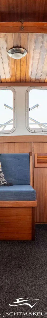 Een interieur van een boot met houten wanden en plafond, blauwe banken, een donkergrijze vloer en ramen met blauwe gordijnen.