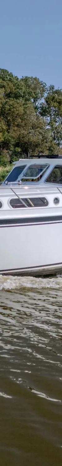 Een witte motorboot met zwarte streep vaart op een waterweg met bomen langs de oever, een persoon is zichtbaar in de…