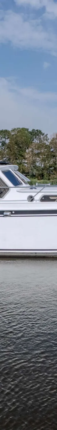 Een witte motorjacht met de naam "Minion" vaart op water, met een zwarte kap en een Nederlandse vlag aan de spiegel.