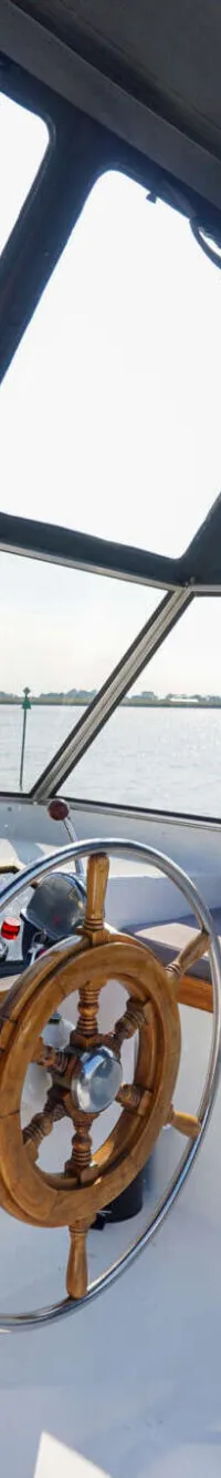 Een houten stuurwiel en dashboard zijn zichtbaar in de open kuip van een boot met grote ramen en een zwarte kap.