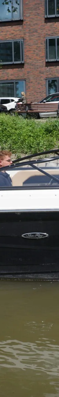 Een witte en zwarte motorboot met beige bekleding vaart op het water, met een persoon aan het stuur en de naam "Vantastic"…