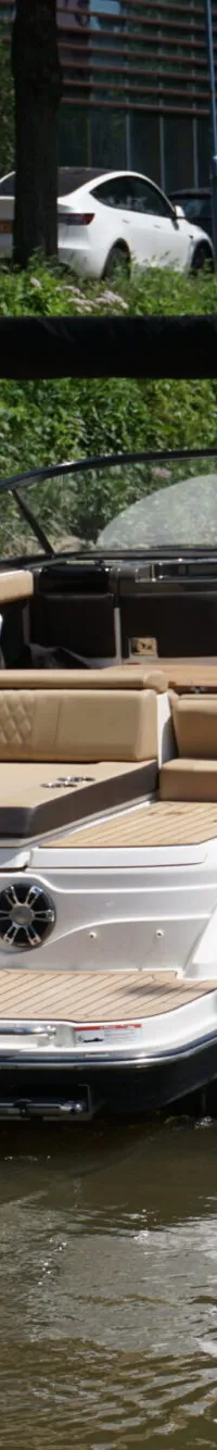 Een witte en donkere boot met een beige interieur en een zwarte biminitop vaart op het water, met een persoon aan het stuur.
