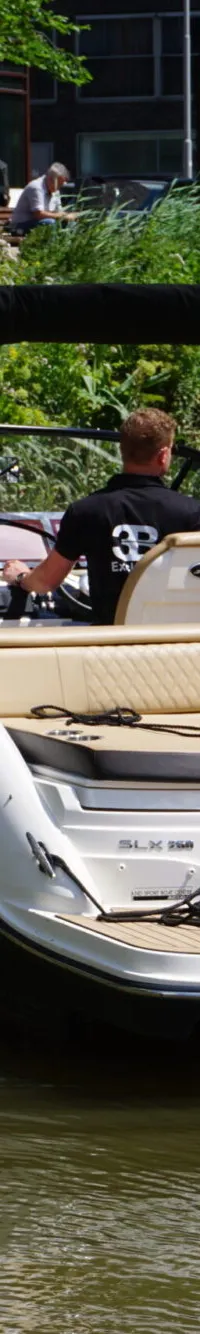 Een witte en donkere boot met een zwarte biminitop en beige bekleding vaart op het water, bestuurd door een persoon.
