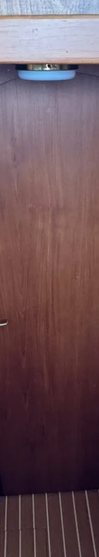 Een interieur van een boot met houten wanden, een blauwe bank met kussens, een brandblusser en een houten deur.