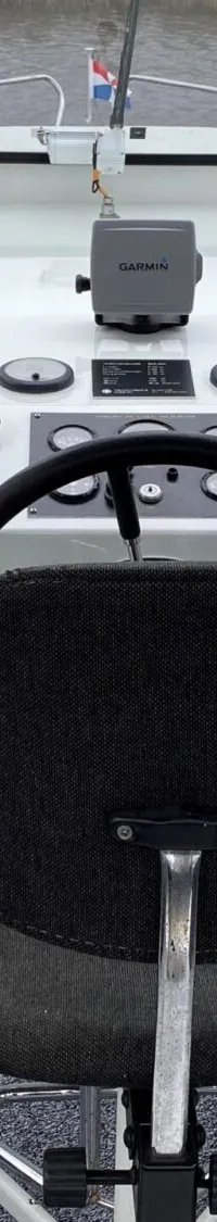 Een stuurhut van een boot met een zwart stuur, een Garmin-apparaat en een houten bankje.