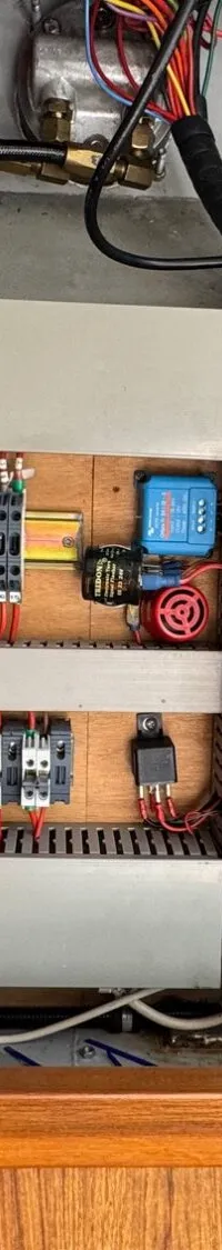 Een detailfoto van een elektrisch paneel met diverse draden, schakelaars en componenten, gemonteerd op een houten…
