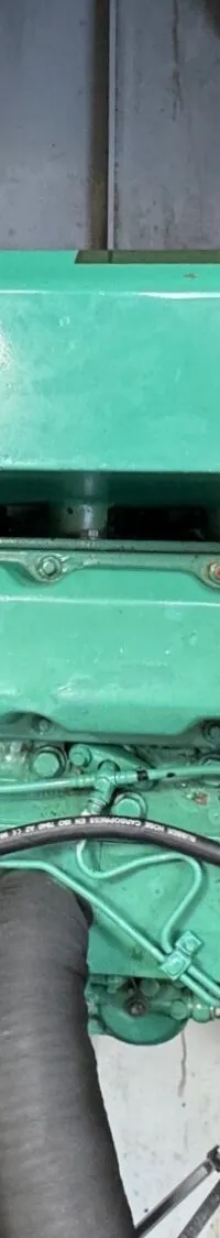 Een groene scheepsmotor met diverse slangen en leidingen is zichtbaar in een motorruimte.