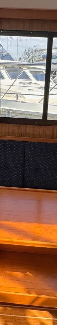 Een interieur van een boot met een houten tafel, blauwe banken en ramen met uitzicht op een andere boot.