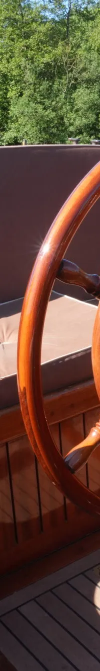 Een houten stuurwiel en een bedieningspaneel met de tekst "HOBELT" zijn zichtbaar in een boot met bruine kussens.