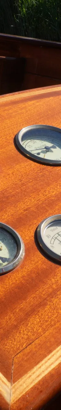 Een houten dashboard met zes ronde meters, een schakelaar en een sleutelhanger met een gloeilampje.
