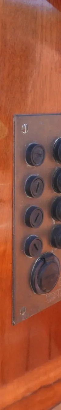 Een houten stuurwiel en een bedieningspaneel met schakelaars en indicatielampjes zijn zichtbaar.
