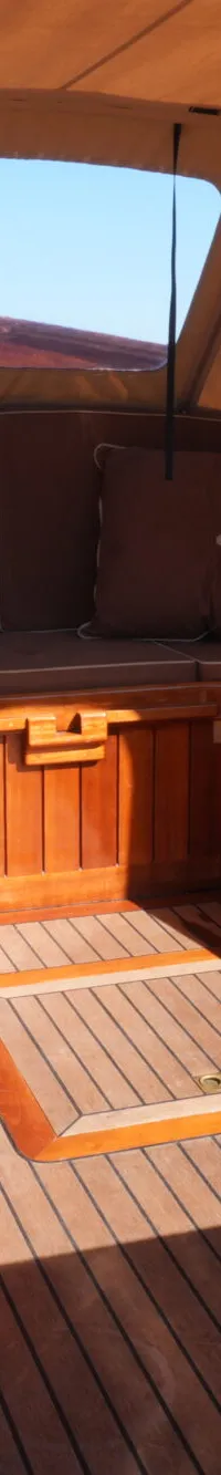 De foto toont de kuip van een boot met houten afwerking, bruine kussens en een beige cabriokap.