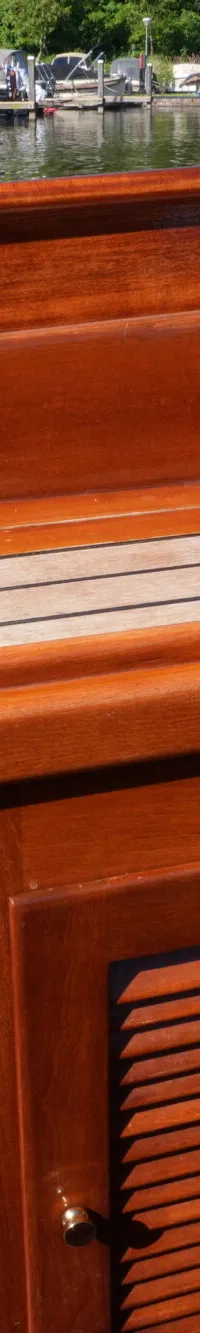 Een close-up van de houten binnenkant van een boot met een bruin kussen en een luik met lamellen.
