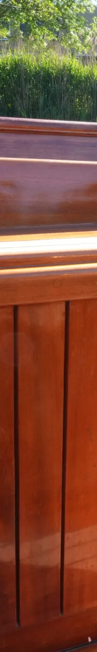 De foto toont een detail van een bootinterieur met glanzend bruin houtwerk en bruine kussens.