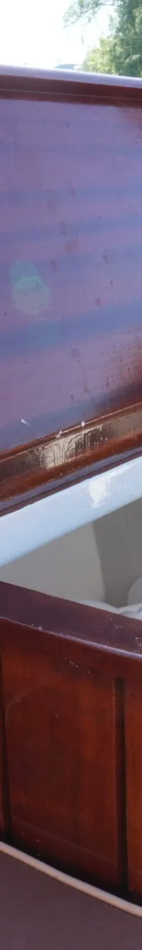 Een open houten kist met een opengeklapt deksel en een witte binnenkant, omringd door bruine kussens en een houten dek.