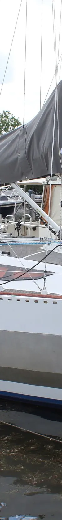 Een witte zeilboot met een grijze streep op de romp en een grijze zeilhoes ligt aangemeerd in een haven. — Ovni 32