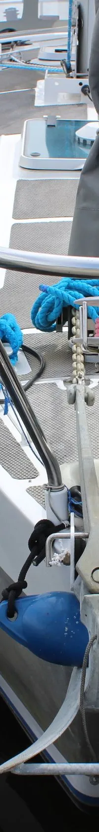 De boeg van een witte zeilboot met blauwe stootwillen en aanmeerlijnen ligt aangemeerd aan een houten steiger. — Ovni 32