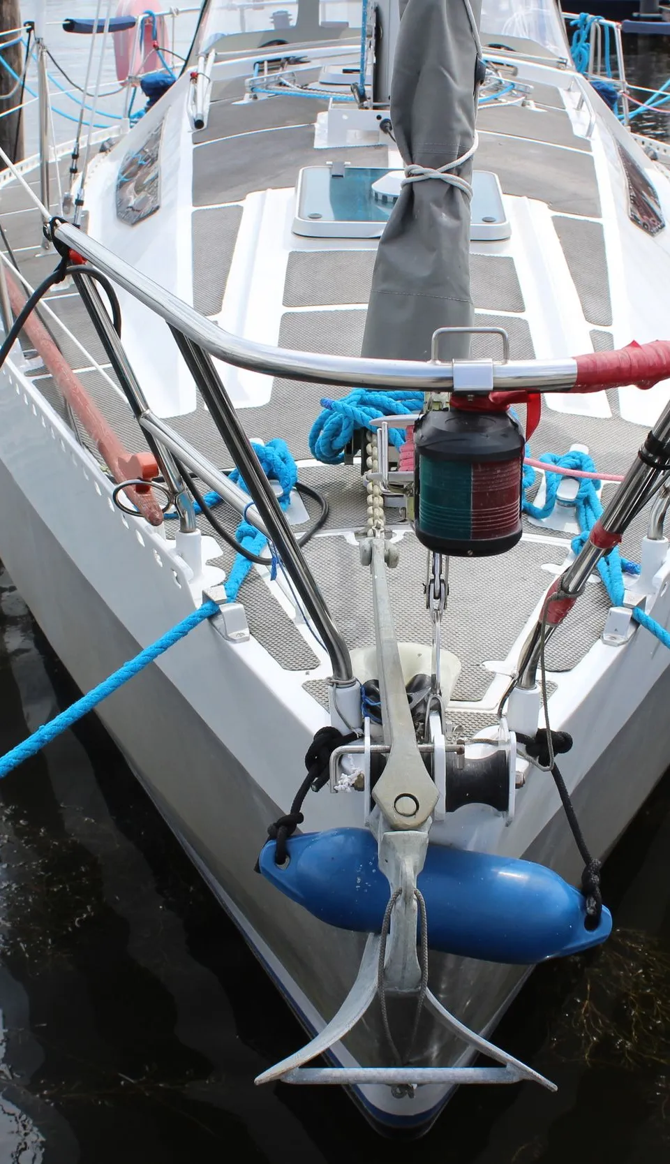 De boeg van een witte zeilboot met blauwe stootwillen en aanmeerlijnen ligt aangemeerd aan een houten steiger. — Ovni 32
