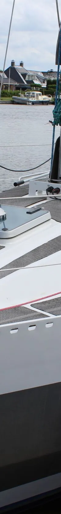Een witte zeilboot met een grijze romp en een grijs zeilhuik ligt afgemeerd aan een houten steiger. — Ovni 32