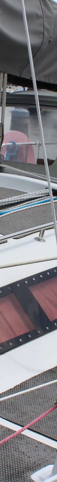 Een witte zeilboot met een grijs dek en een grijze buiskap ligt in een haven, met diverse lijnen en stootwillen zichtbaar.