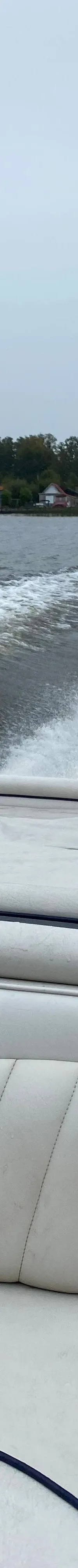 De achterkant van een boot met witte bekleding en een houten handgreep, die een kielzog achterlaat op het water.