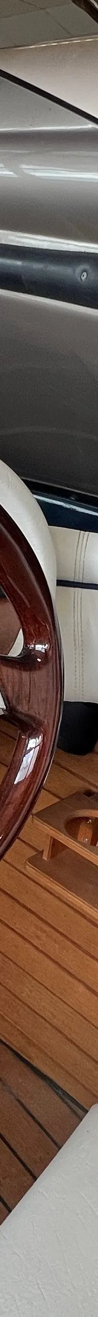 Een houten stuurwiel met chromen spaken en een houten dashboard met diverse meters zijn zichtbaar.