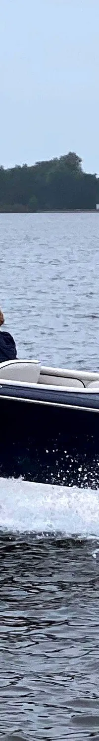 Een donkerblauwe speedboot met een witte onderkant vaart over het water, met een persoon aan het stuur.