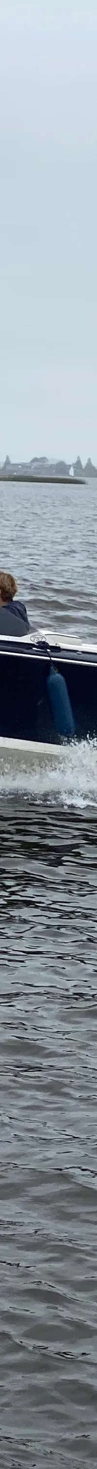 Een donkerblauwe speedboot met een witte onderkant vaart over het water, met een persoon aan het roer.