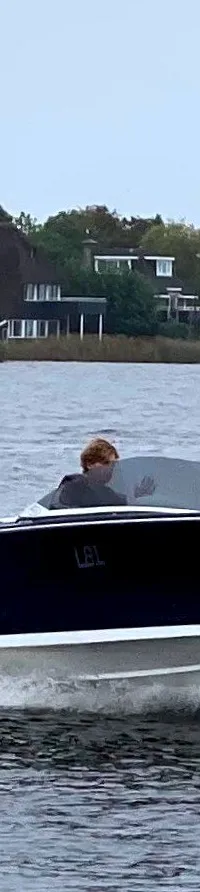 Een donkerblauwe speedboot met een witte onderkant vaart over het water, met een persoon aan het roer.