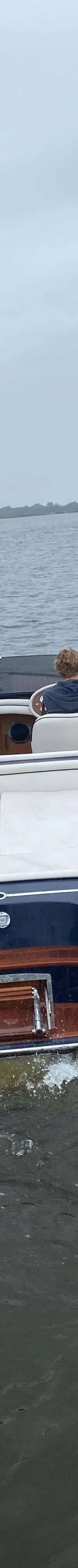 Een blauwe speedboot met houten accenten en witte bekleding vaart op een meer onder een bewolkte hemel.