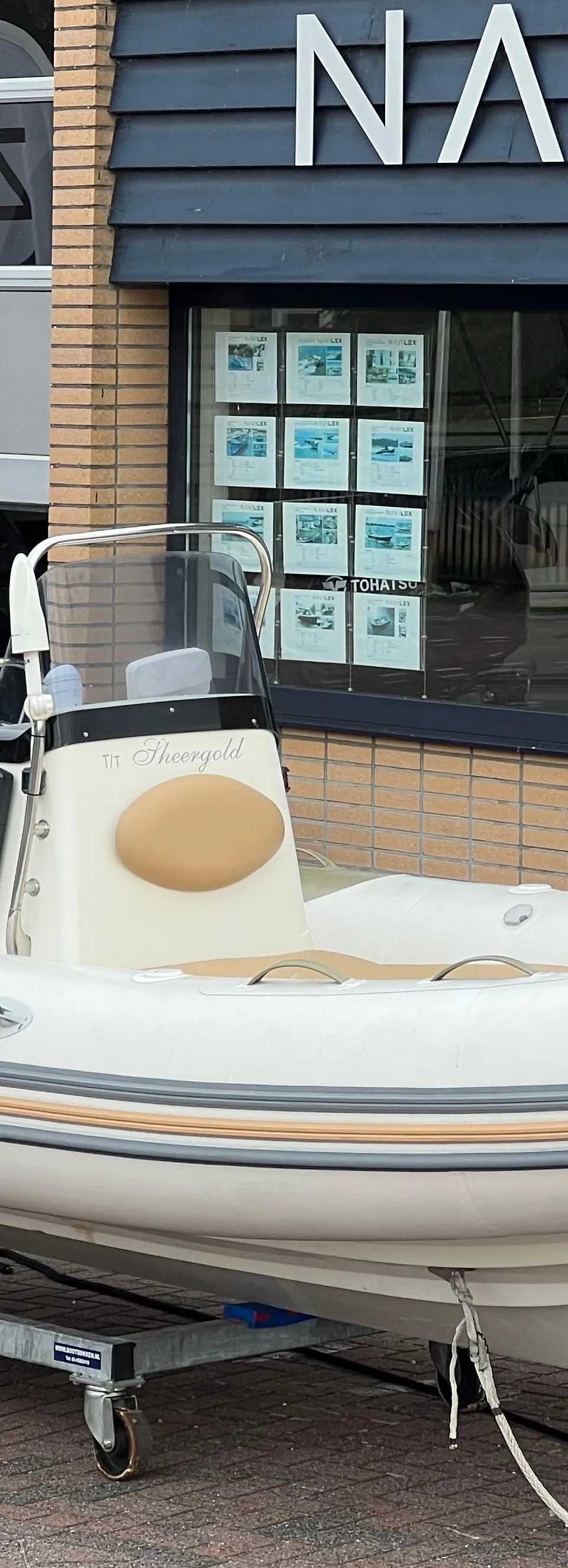 Een witte rubberboot met een Yamaha buitenboordmotor staat op een trailer voor een gebouw met de tekst "NAVILEX".