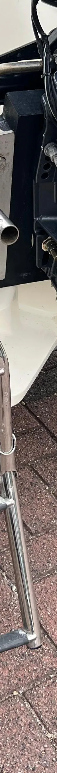 Een boot met een grijze buitenboordmotor en een opklapbare zwemtrap met houten treden, staand op een bakstenen ondergrond.