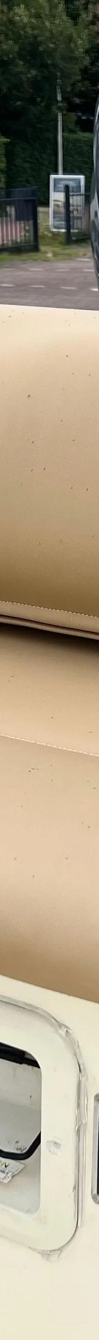 Een boot met beige kussens en een buitenboordmotor, met op de achtergrond een huis en geparkeerde auto's.