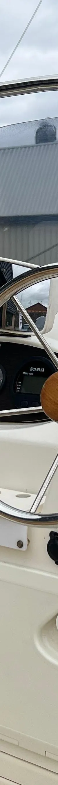 Een witte consoleboot met een stuurwiel, kompas, Yamaha-bediening en een VHF-antenne, geparkeerd bij een gebouw.